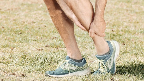 Runner standing on grass, holding the back of their calf