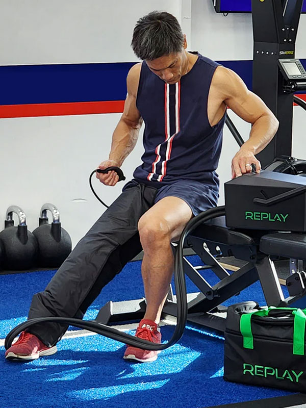 Man on a gym bench with a REPLAY compression unit's hose connected to his leg